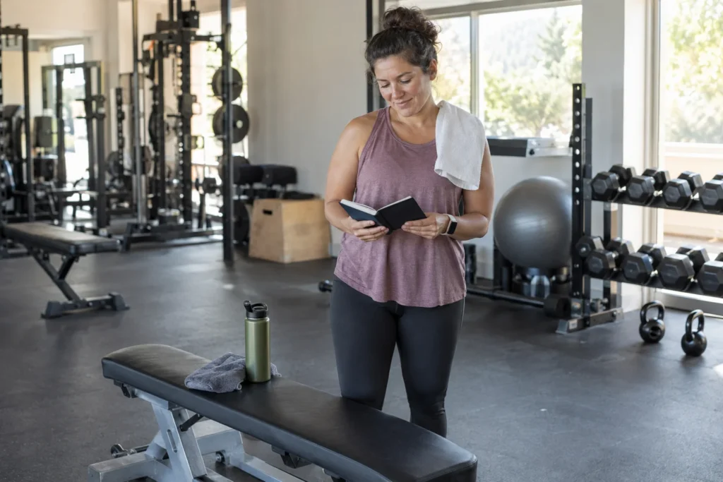 Una persona vuelve al gimnasio y consulta con calma su libreta antes de empezar una sesión de fuerza.